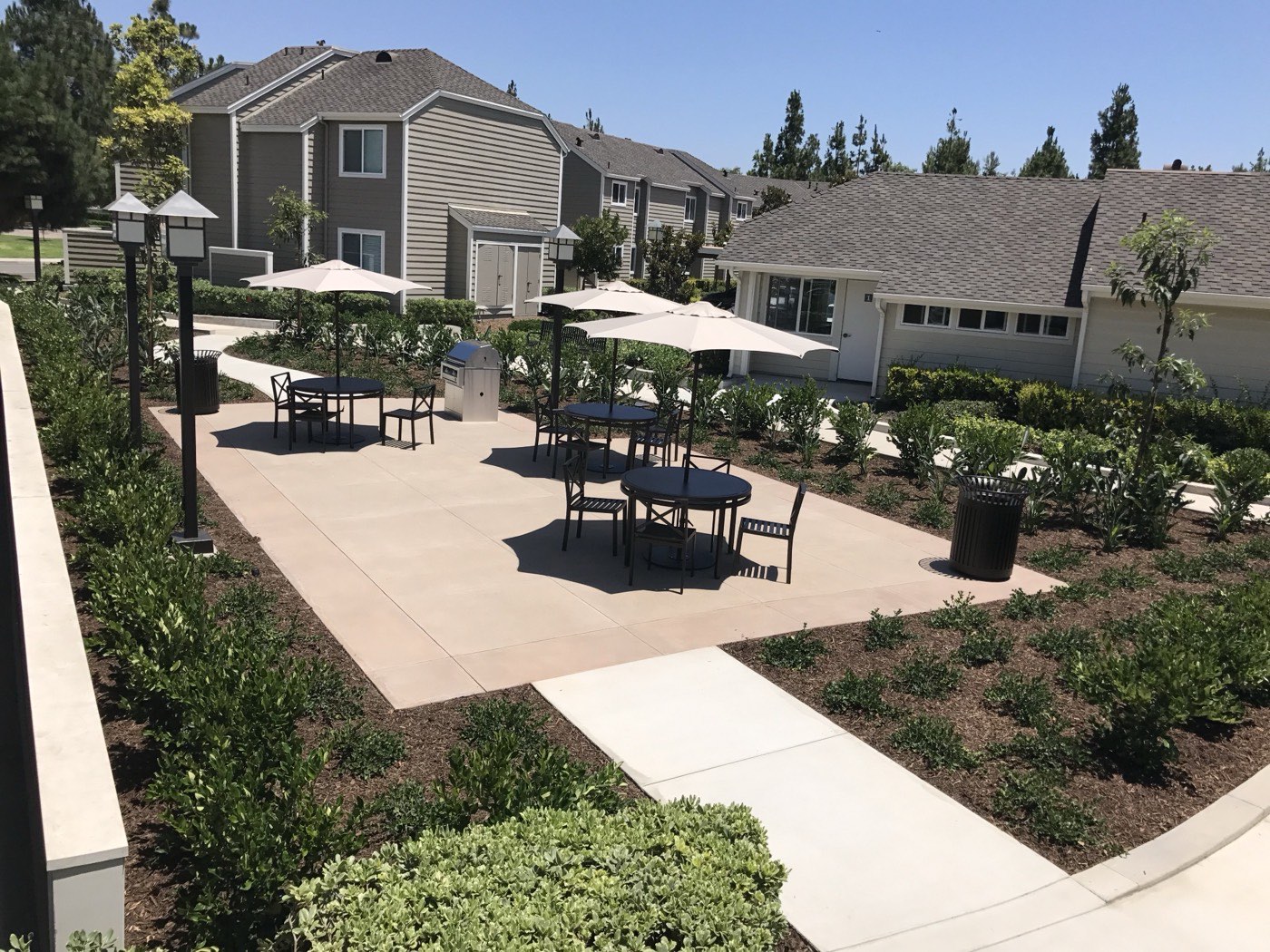 New concrete patio with umbrella-shaded seating at a multifamily community, viewed from an elevated angle